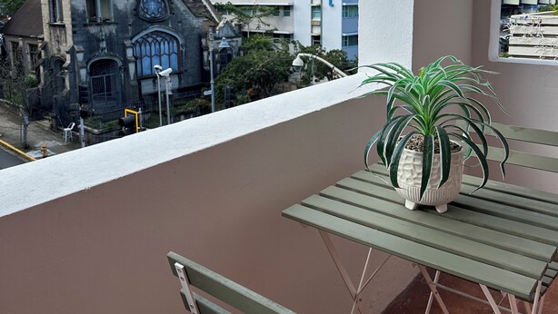 A balcony with a potted plant, a table, and a bench. In the background, there is a hotel with a sign that reads "HOTEL" and a building with a gothic architectural style. - Renovated & Authentic San Juan 1-Bedroom APT w/ Caribbean Views (San Juan)