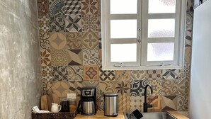 A compact kitchen with a tiled backsplash, a window above the sink, and a countertop with a coffee maker and kettle. - Renovated & Authentic San Juan 1-Bedroom APT w/ Caribbean Views (San Juan)