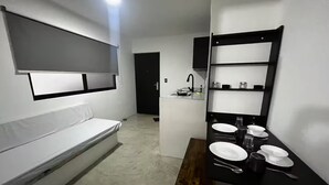 Une pièce de taille modeste comprenant un lit, une petite table avec un miroir et un coin cuisine.