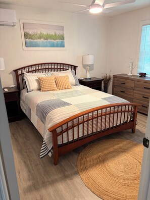 Ein Schlafzimmer mit einem hölzernen Bett, Nachttischen, einem Nachttisch, einer Lampe, einer Uhr, einer Kommode, einem Gemälde und einem Teppich.