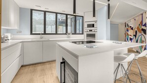 Eine moderne Küche mit weißen Schränken, einer zentralen Kochinsel mit Sitzgelegenheiten, einem großen Fenster und einer Mikrowelle.