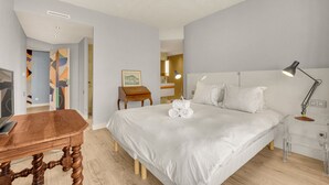 Ein modernes Hotelzimmer mit einem großen Bett, einem Holztisch und einem klaren Nachttisch.