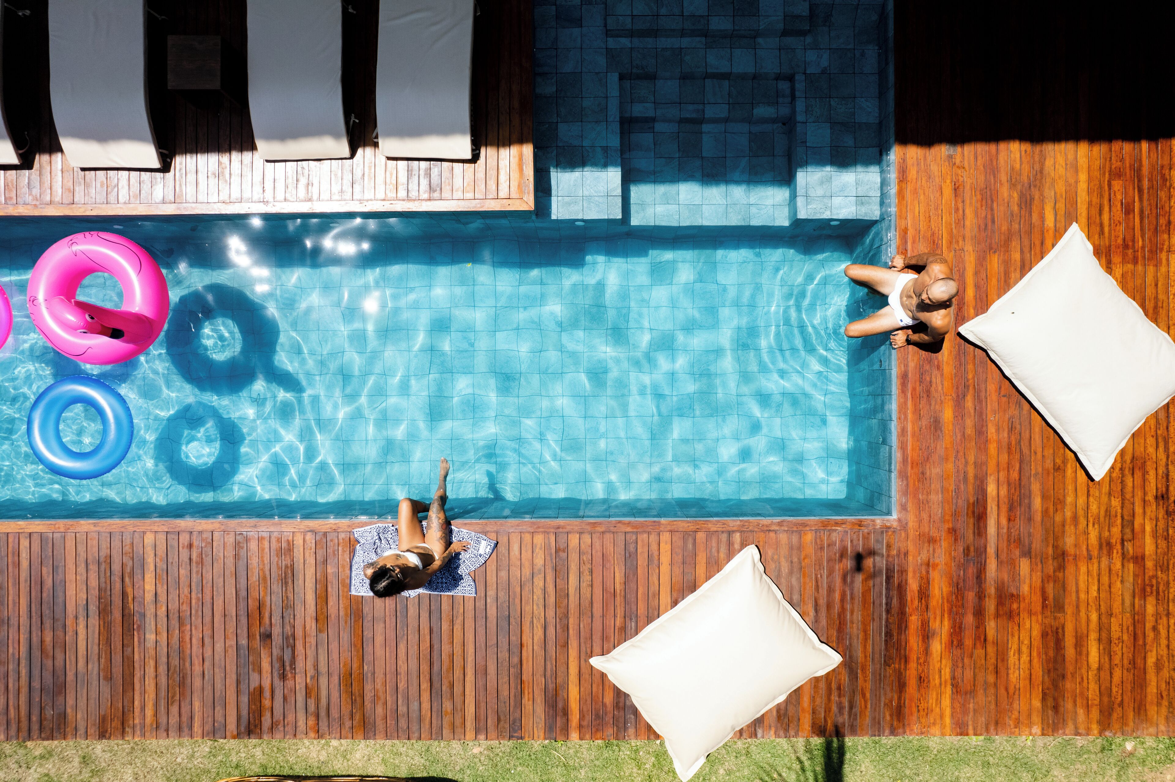 A rooftop pool with wooden decking, lounge chairs, and inflatable rings.