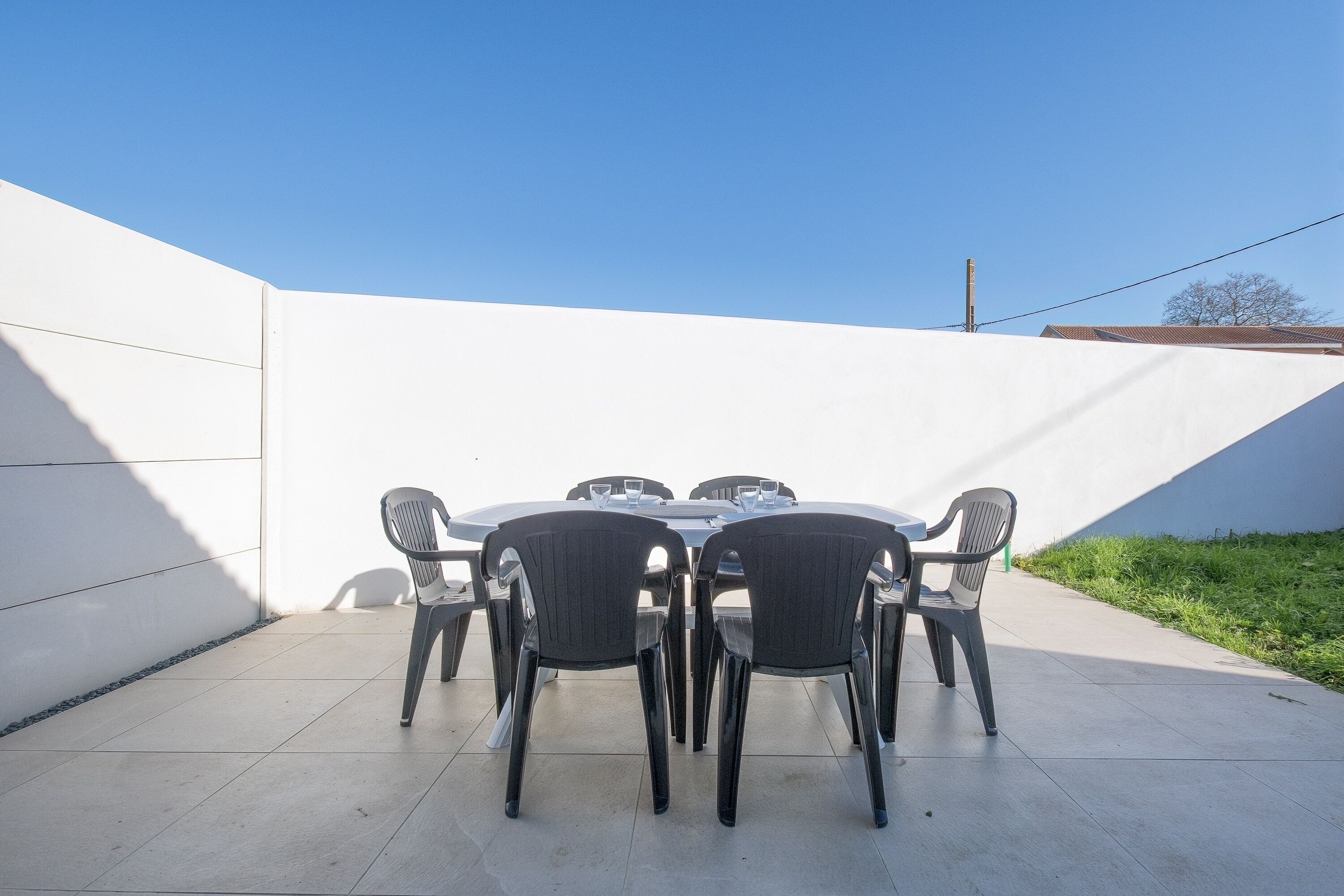 Un espace patio avec une table ronde et six chaises, entouré d’un mur blanc et surmonté d’un toit en pente.