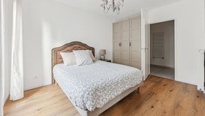 Ein Schlafzimmer mit einem hölzernen Bett, weißer Bettwäsche, einer Chandelieber und einem Kleiderschrank.