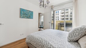 Ein Schlafzimmer mit einem Bett, einer Chandelier, einem Gemälde und Blick auf ein Gebäude durch eine Glastür.