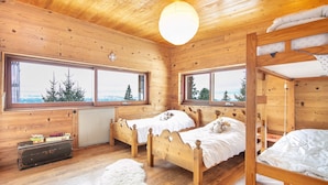 A wooden cabin room with two beds, a radiator, and a view of trees through large windows. - La Perchette - Joli chalet classé 3* (Chamrousse)