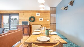 A dining area with wooden furniture, a table set for four, and a view through a glass door. - La Perchette - Joli chalet classé 3* (Chamrousse)