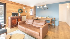 A cozy living room with a leather couch, wooden cabinet, and a dining area with a table and chairs. - La Perchette - Joli chalet classé 3* (Chamrousse)