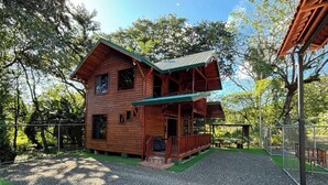 Eine Holzhütte mit Veranda und überdachter Terrasse, umgeben von Bäumen und einer Schotterzufahrt.