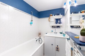 A bathroom with a white bathtub, a sink, and a mirror. There are toiletries on the counter and a showerhead above the bathtub.