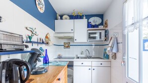 Una cocina compacta con gabinetes blancos, microondas, hervidor y pileta.