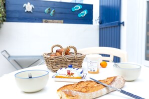 A table with a loaf of bread, a knife, a bowl, a container of butter, and a basket of bread.