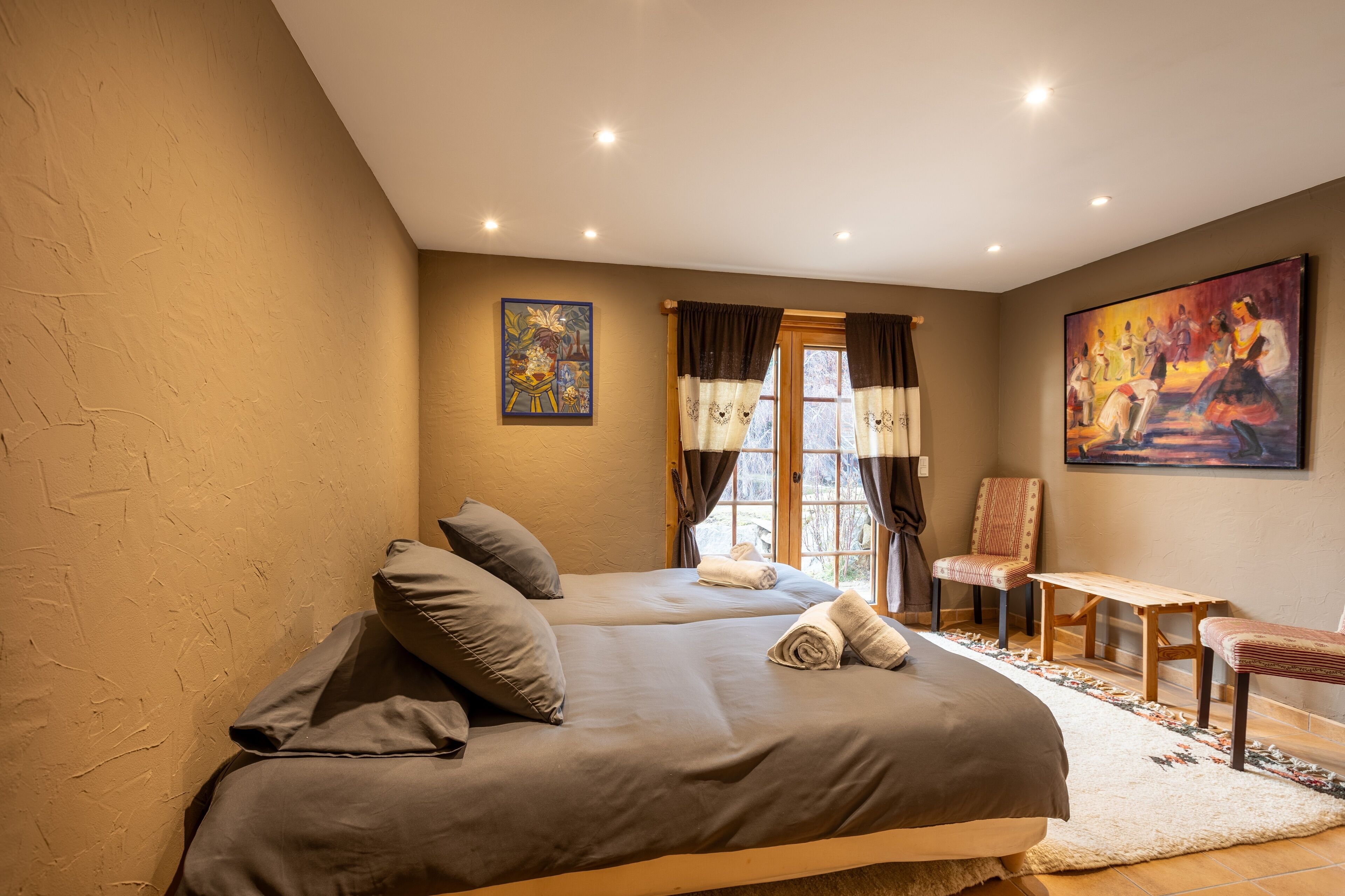 A bedroom with two beds, a chair, a small table, and artwork on the walls.