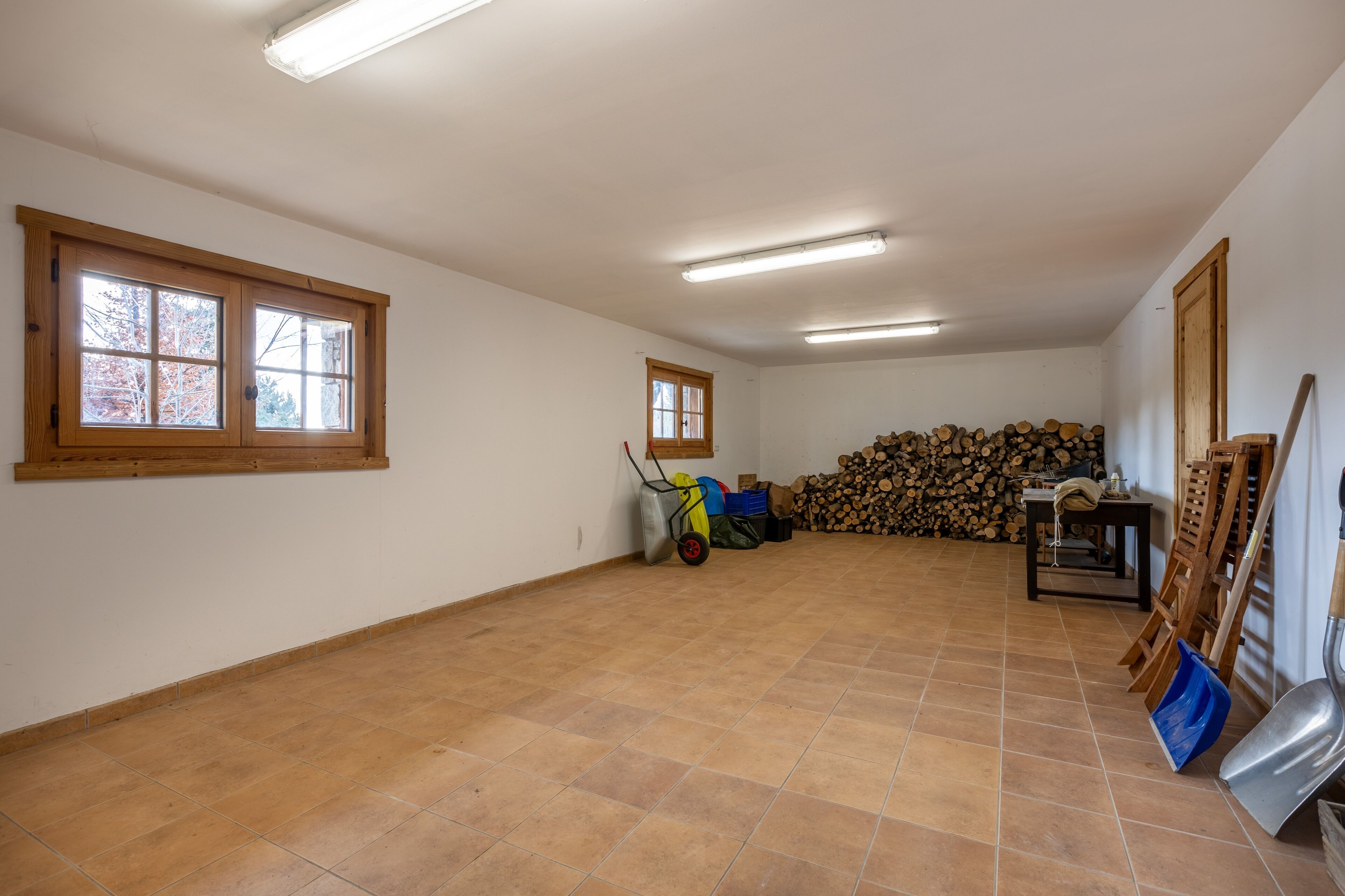 A spacious room with two windows, a ceiling fan, and a stack of firewood.