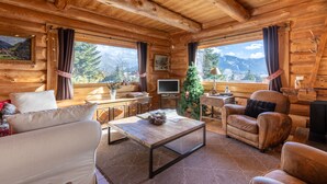 A cozy log cabin interior with a wooden ceiling, a television, a Christmas tree, and a view of mountains through large windows. - Chalet des Sonnailles - Montagnes, jardin et garage (Bolquère)