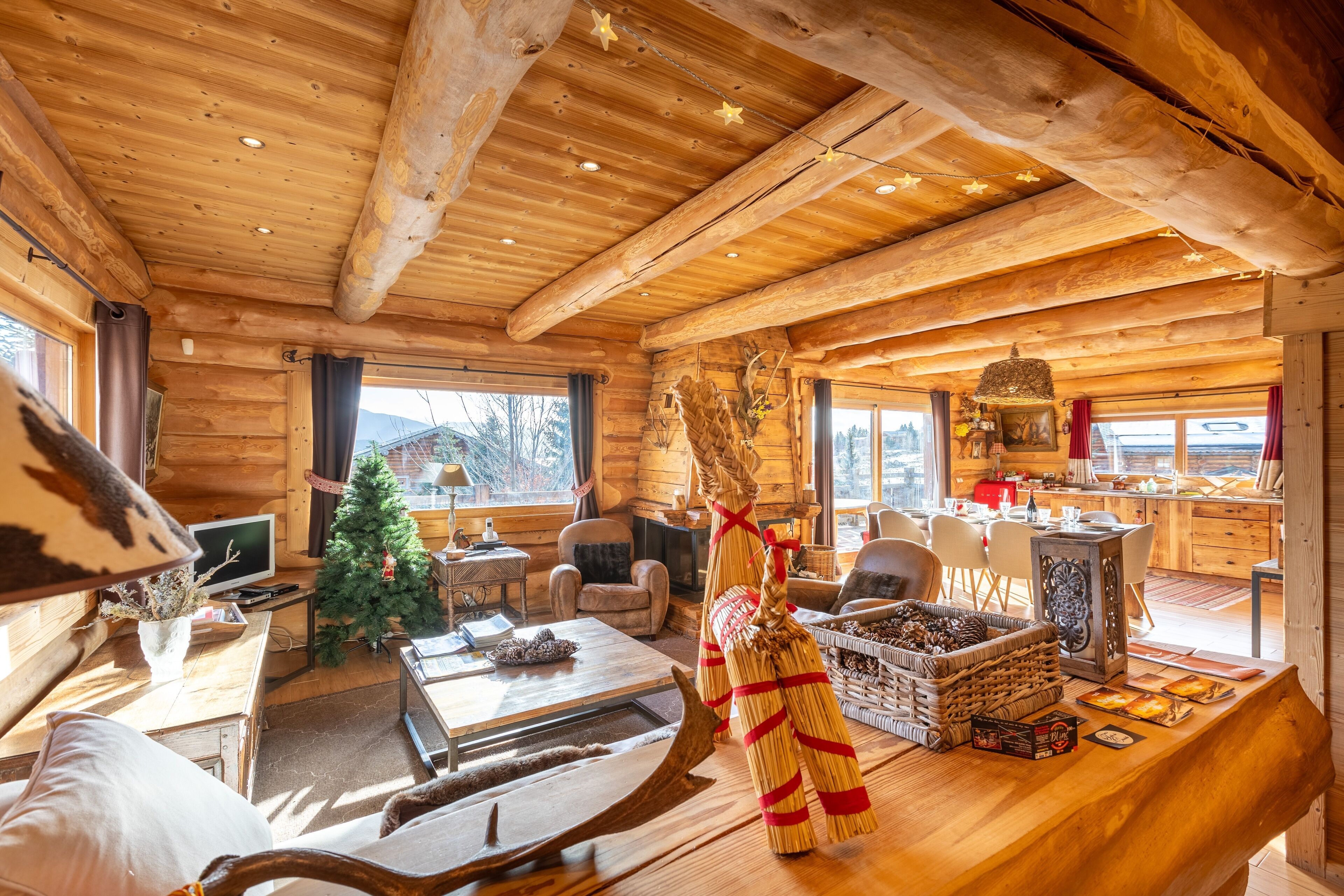 Een gezellig interieur van een blokhut, met een open haard, houten meubels, een kerstboom en een keukenhoek.