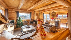 A cozy log cabin interior with a fireplace, wooden furniture, a Christmas tree, and a kitchen area. - Chalet des Sonnailles - Montagnes, jardin et garage (Bolquère)