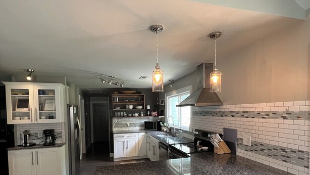 A modern kitchen with granite countertops, white cabinetry, and a central island with stools.