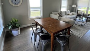 A dining area with a wooden table and chairs, a potted plant, and a clock on the wall.