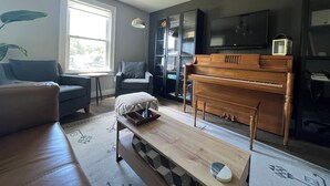 A living room with a piano, a sofa, a coffee table, and a television.