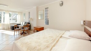 Habitación de hotel con una cama grande, un escritorio con silla, una lámpara y una ventana con cortinas.
