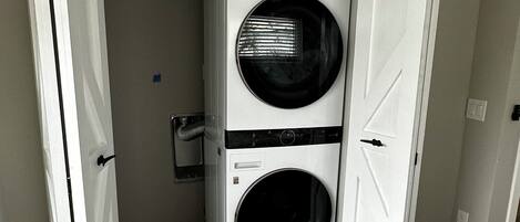 A laundry room with two stacked front-loading washers and dryers, a wooden floor, and a white door.