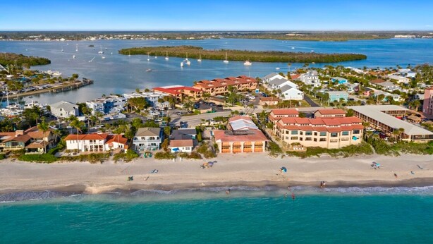 Vista aérea de un pueblo costero con propiedades frente a la playa, un puerto deportivo y aguas azul turquesa.