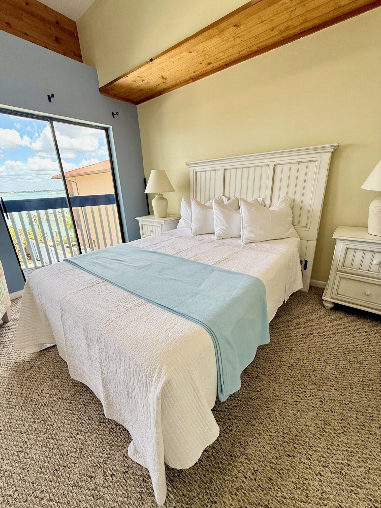 A bedroom with a large bed, two bedside tables, a window with a view, and a wooden ceiling beam.