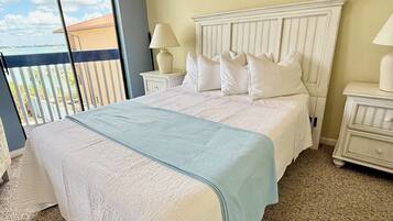 A bedroom with a large bed, two bedside tables, a window with a view, and a wooden ceiling beam.