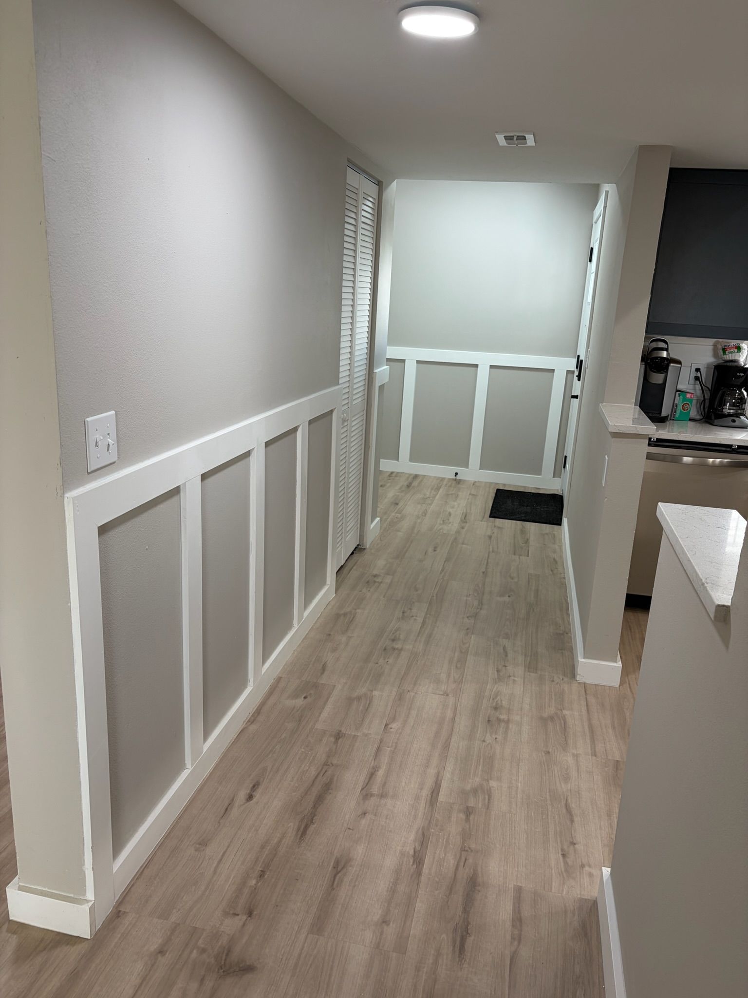 A hallway with a wooden floor, white walls, and a white door at the end.