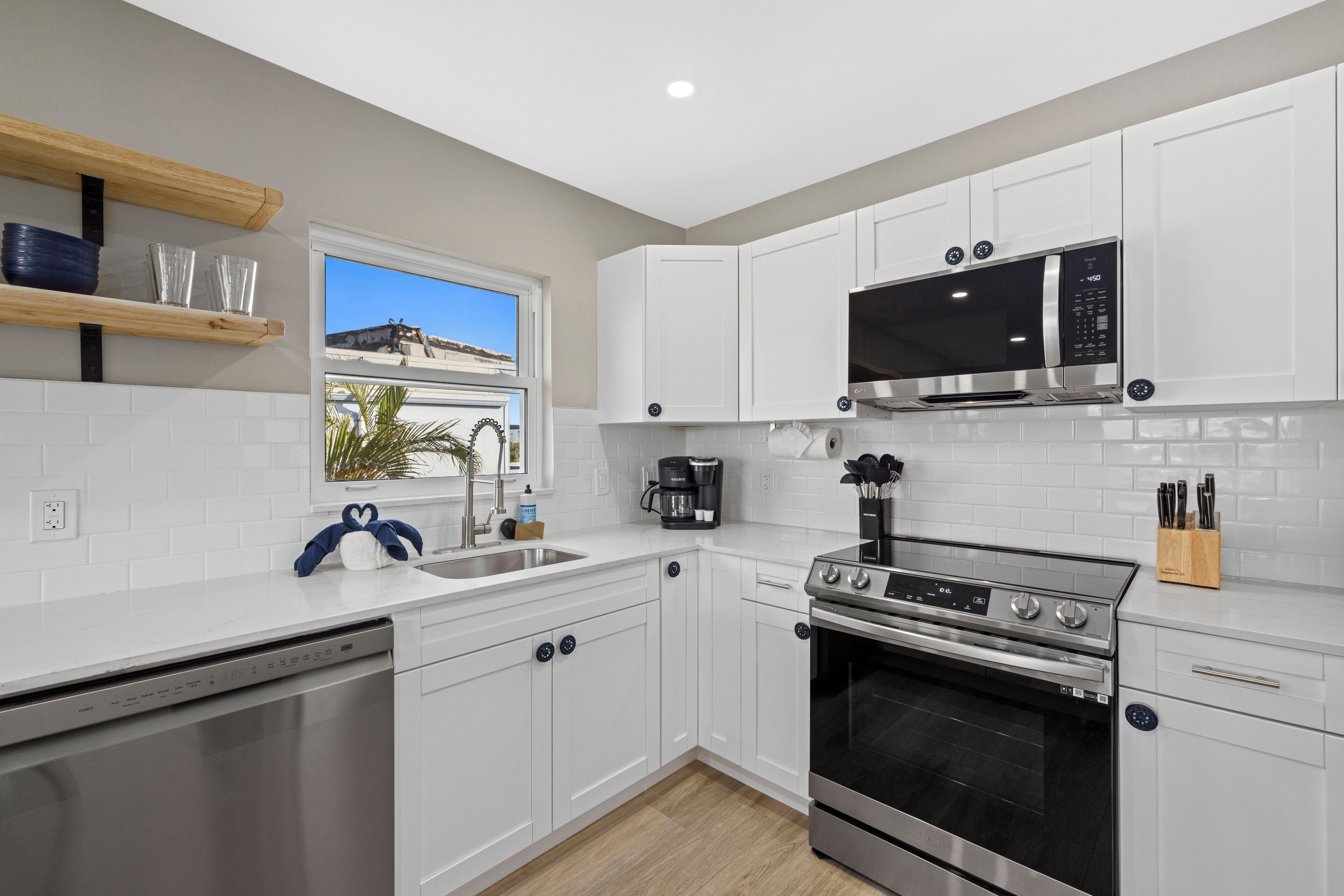 A modern kitchen with white cabinets, a stainless steel dishwasher, a built-in oven, a microwave, and a coffee maker.