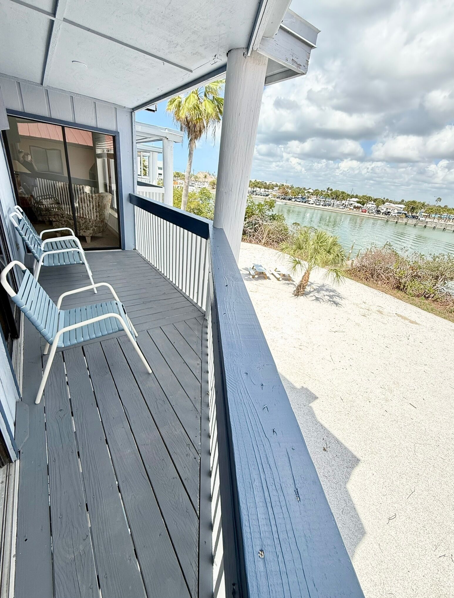 Une terrasse en bois avec des chaises longues, un espace abrité et une vue sur une étendue d’eau et des bâtiments.