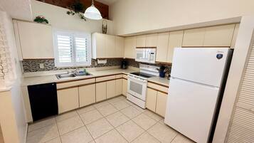 Una cocina con gabinetes blancos, un lavamanos doble, una estufa, un microondas y un refrigerador.