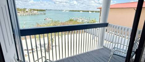 A covered balcony with a view of the sea, a railing, and two chairs.