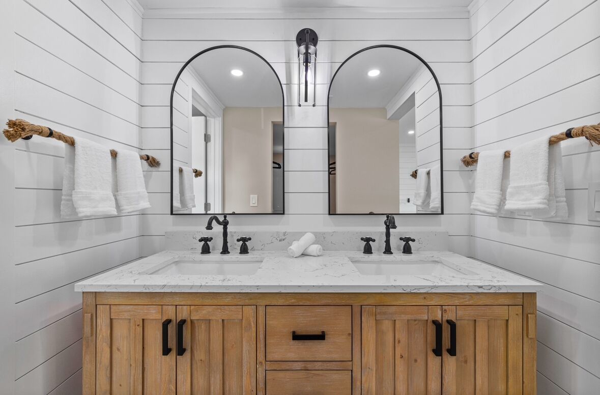 A bathroom with a white marble sink, wooden cabinets, and two large mirrors.