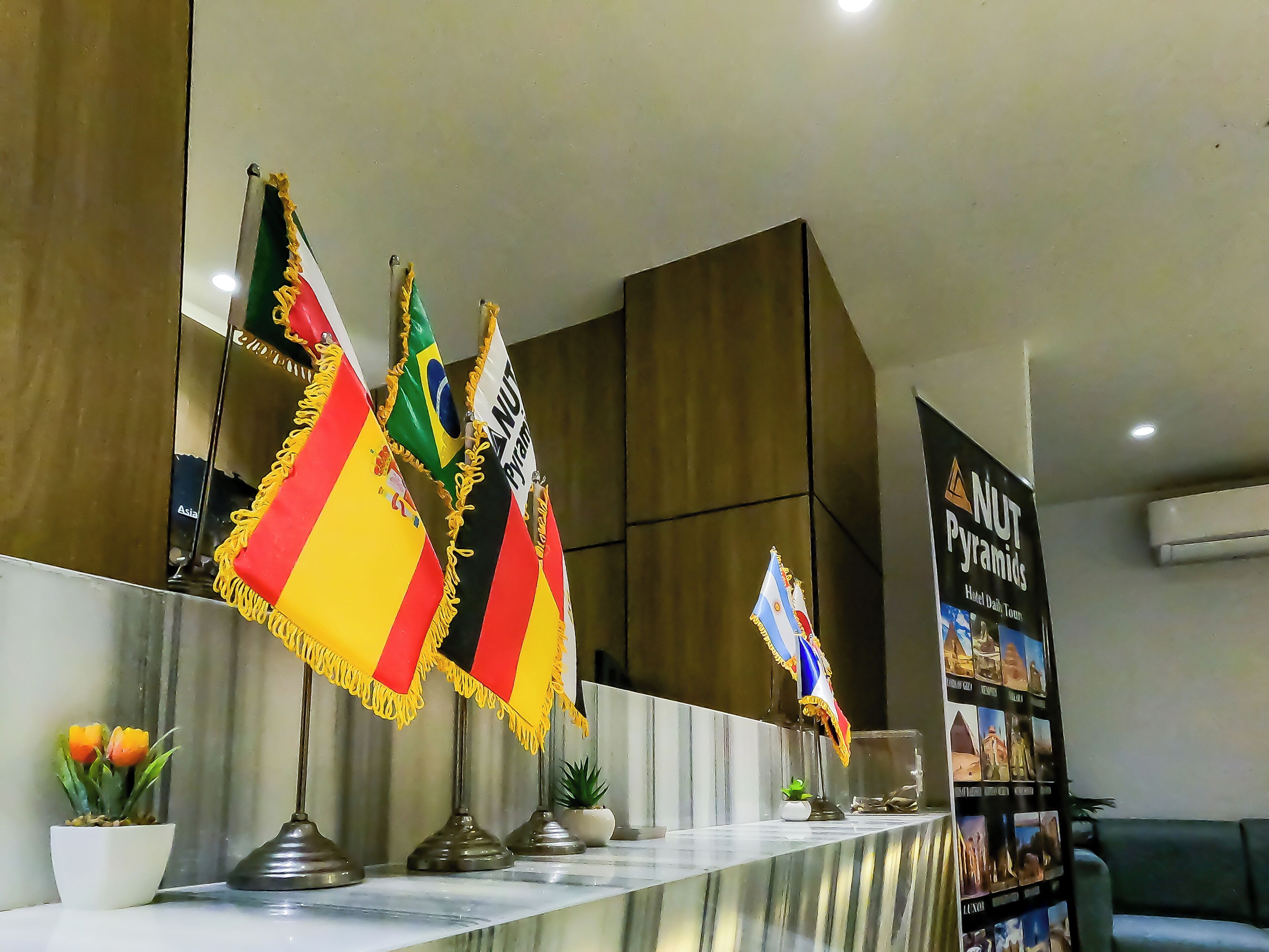 A reception area with multiple flags, a reception desk, and a wall displaying a hotel tour.