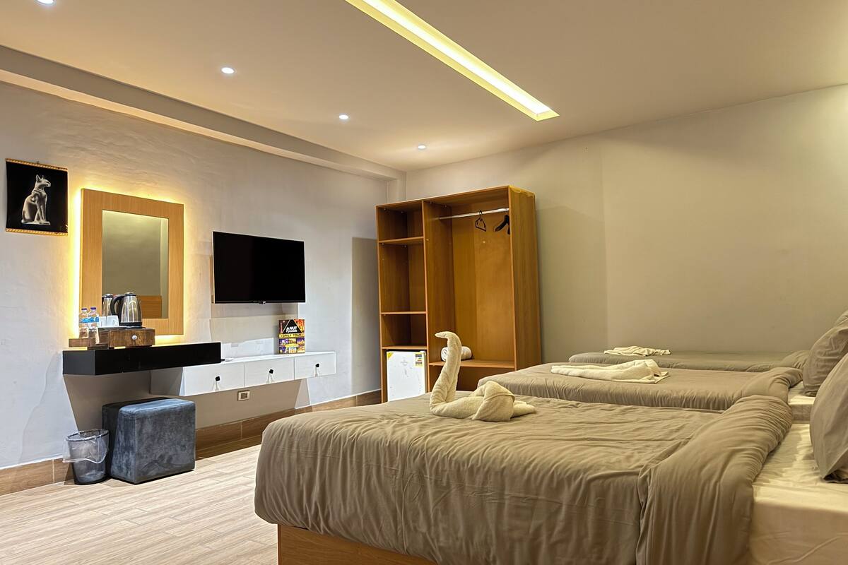 A modern hotel room with two beds, a wooden wardrobe, a vanity with a mirror, a flat-screen TV, and a small table with toiletries.