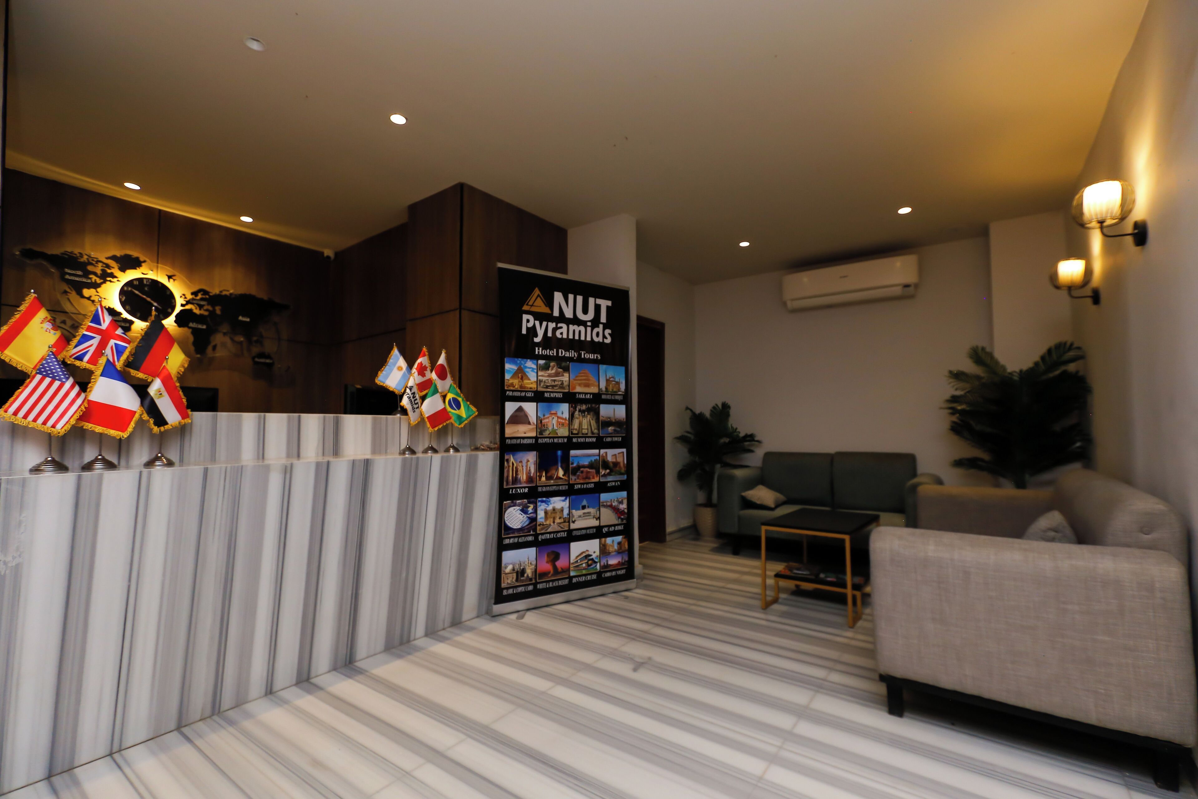 A reception area with a marble floor, a sofa, a small table, and a wall with flags and a 'NUT Pyramids' sign.