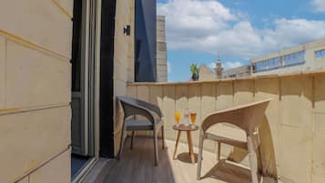 A balcony with two wicker chairs, a small table with drinks, and a view of a building with a tower.