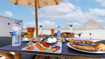 An outdoor dining table with food and drinks, set against a backdrop of a pyramid and clear sky.