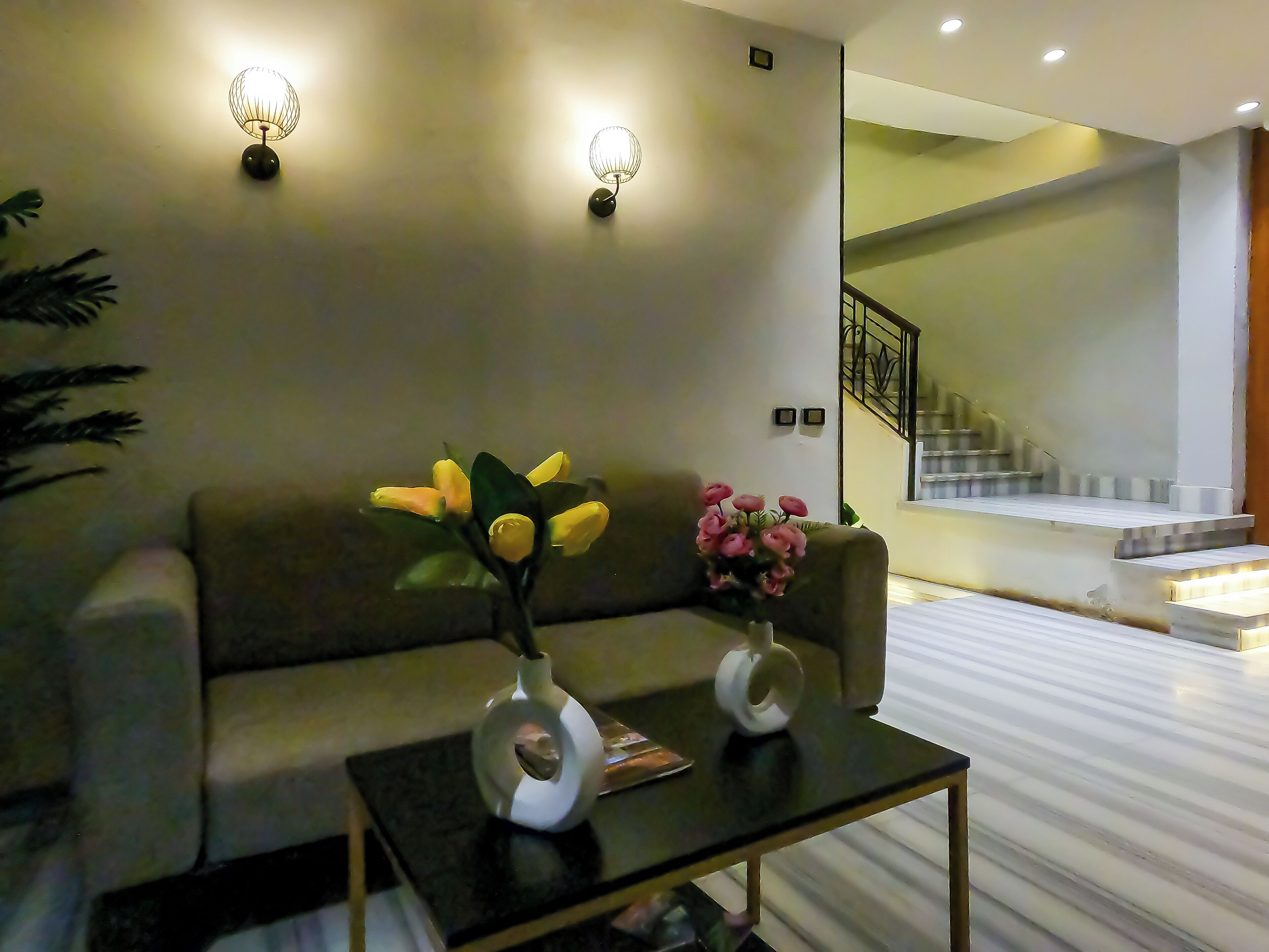 A modern living room with a sofa, two vases with flowers, a coffee table, and a staircase leading to an upper level.