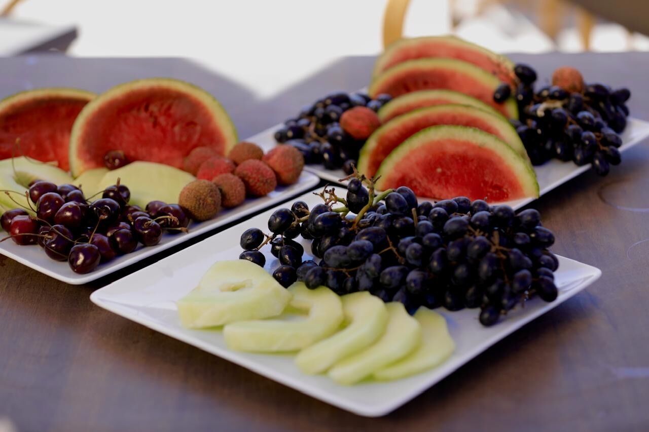 Une assiette de fruits comprenant de la pastèque, des raisins, des cerises et des tranches de pomme.