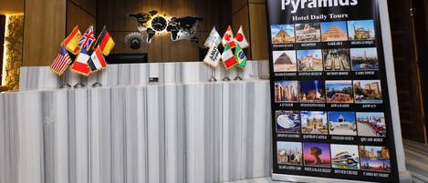 A reception desk with flags, a world map, and a sign for 'NUT Pyramids Hotel Daily Tours' listing various tour destinations.