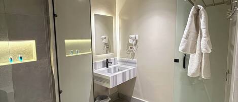 A modern bathroom with a glass shower enclosure, a marble-tiled floor, a glass-enclosed toilet, and a white towel hanging on a rack.