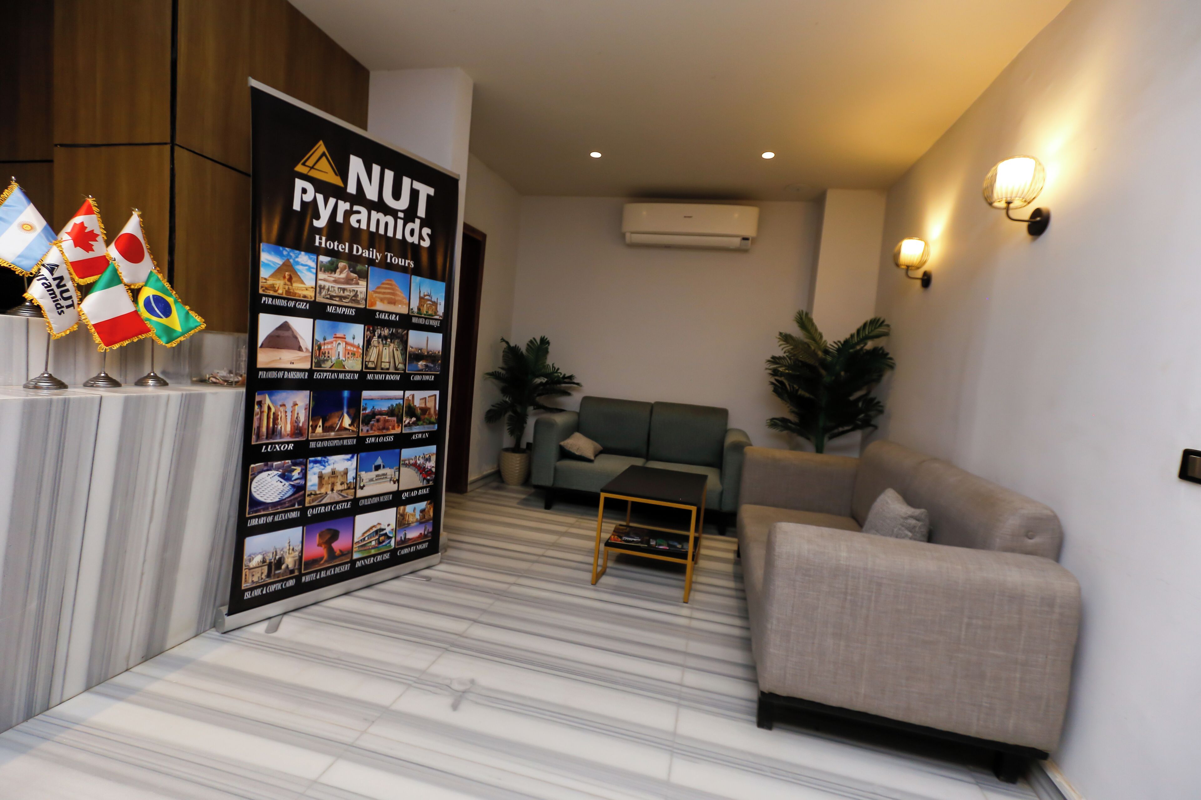 A hotel lobby with a reception desk, a green sofa, a small table, and a wall-mounted air conditioner.