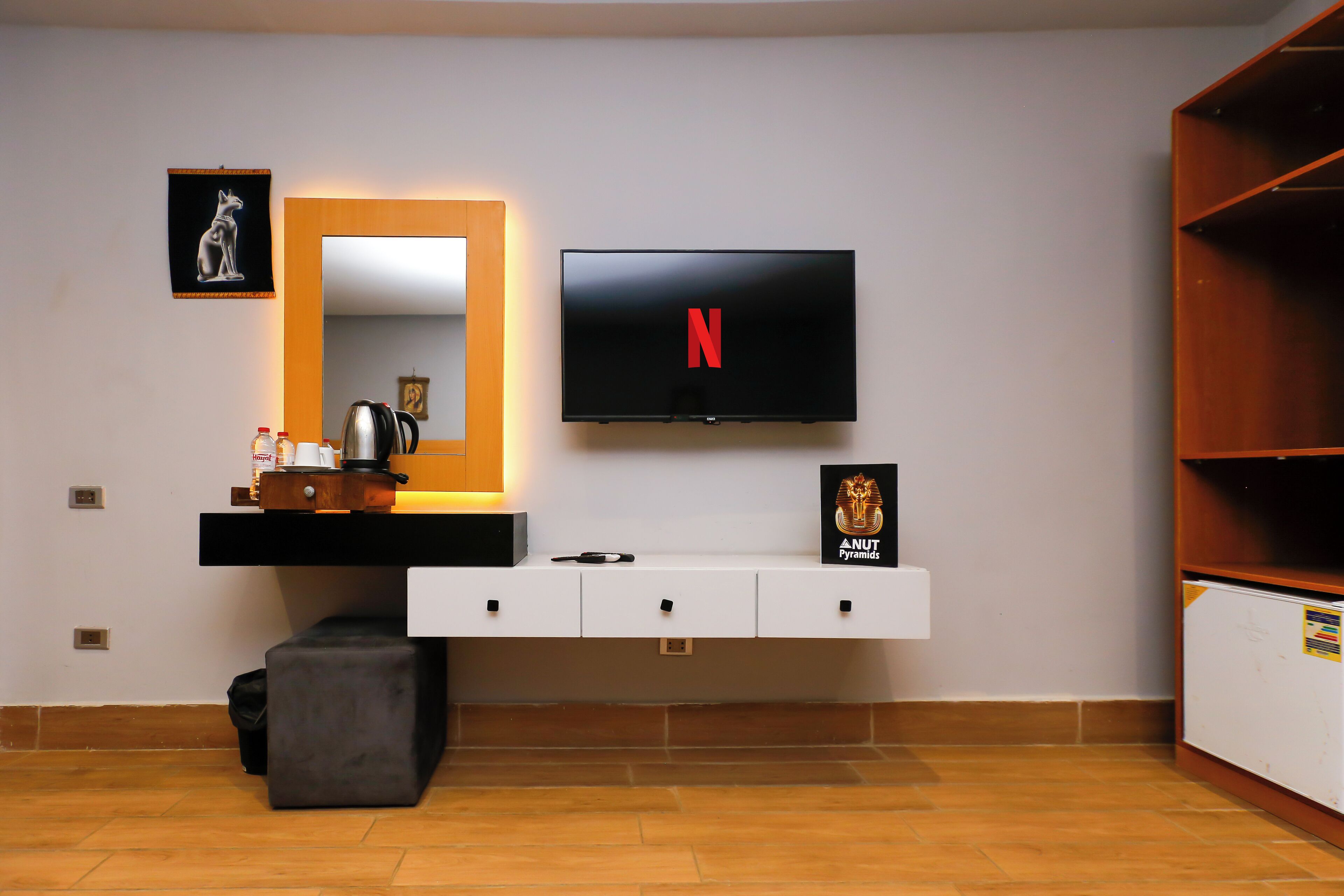 Una sala moderna con un televisor de pantalla plana montado en la pared, una cafetera, un mueble bajo con cajones y un banco.