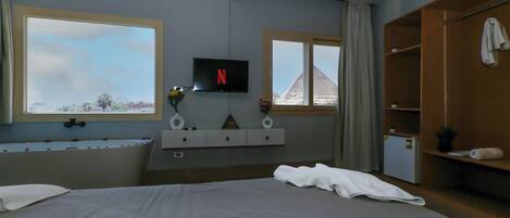 A hotel room with a large bed, a TV mounted on the wall, a bathtub, and a wardrobe.