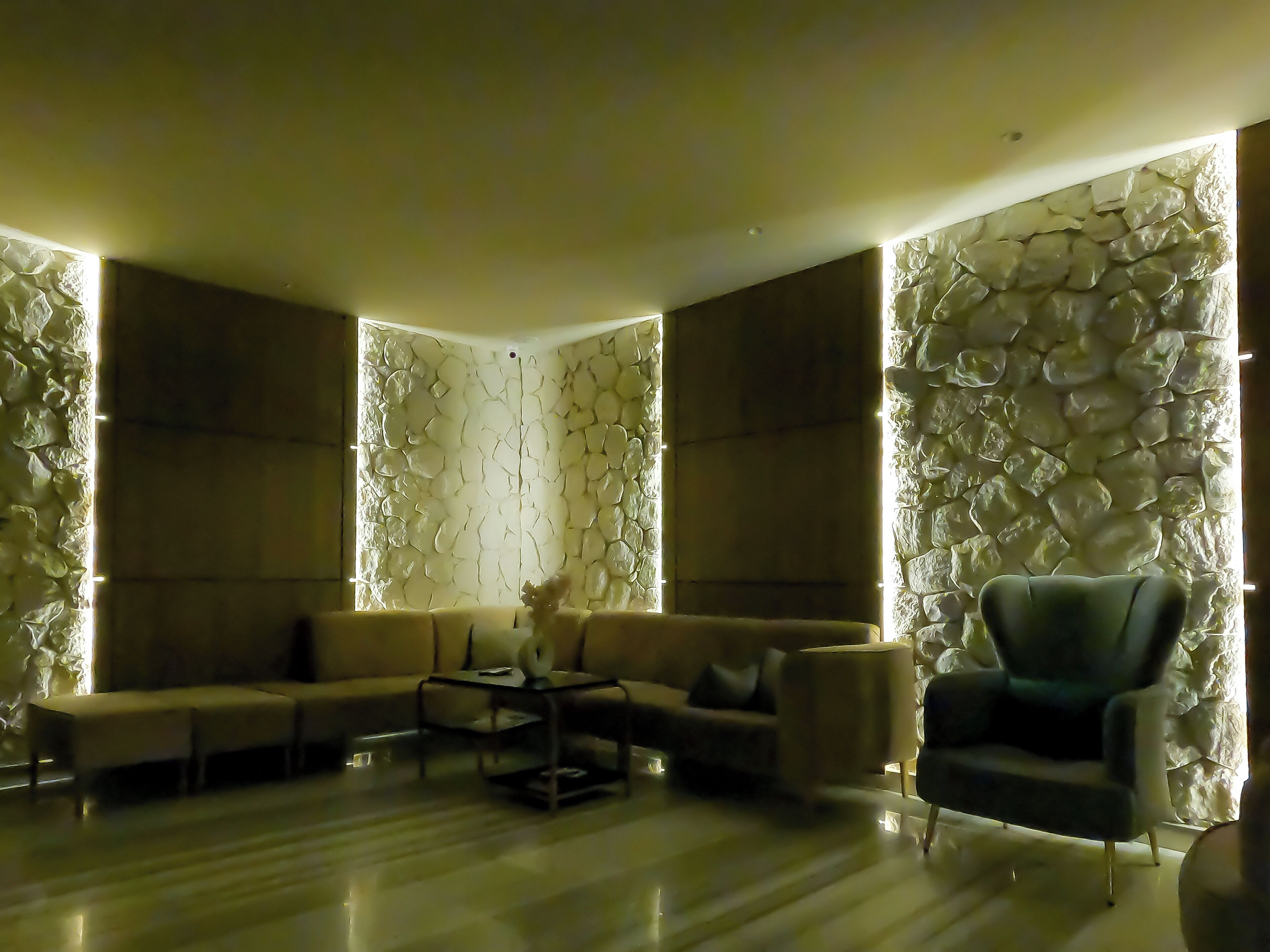 A modern living room with a sectional sofa, a coffee table, and a blue armchair. The walls have a textured stone design.