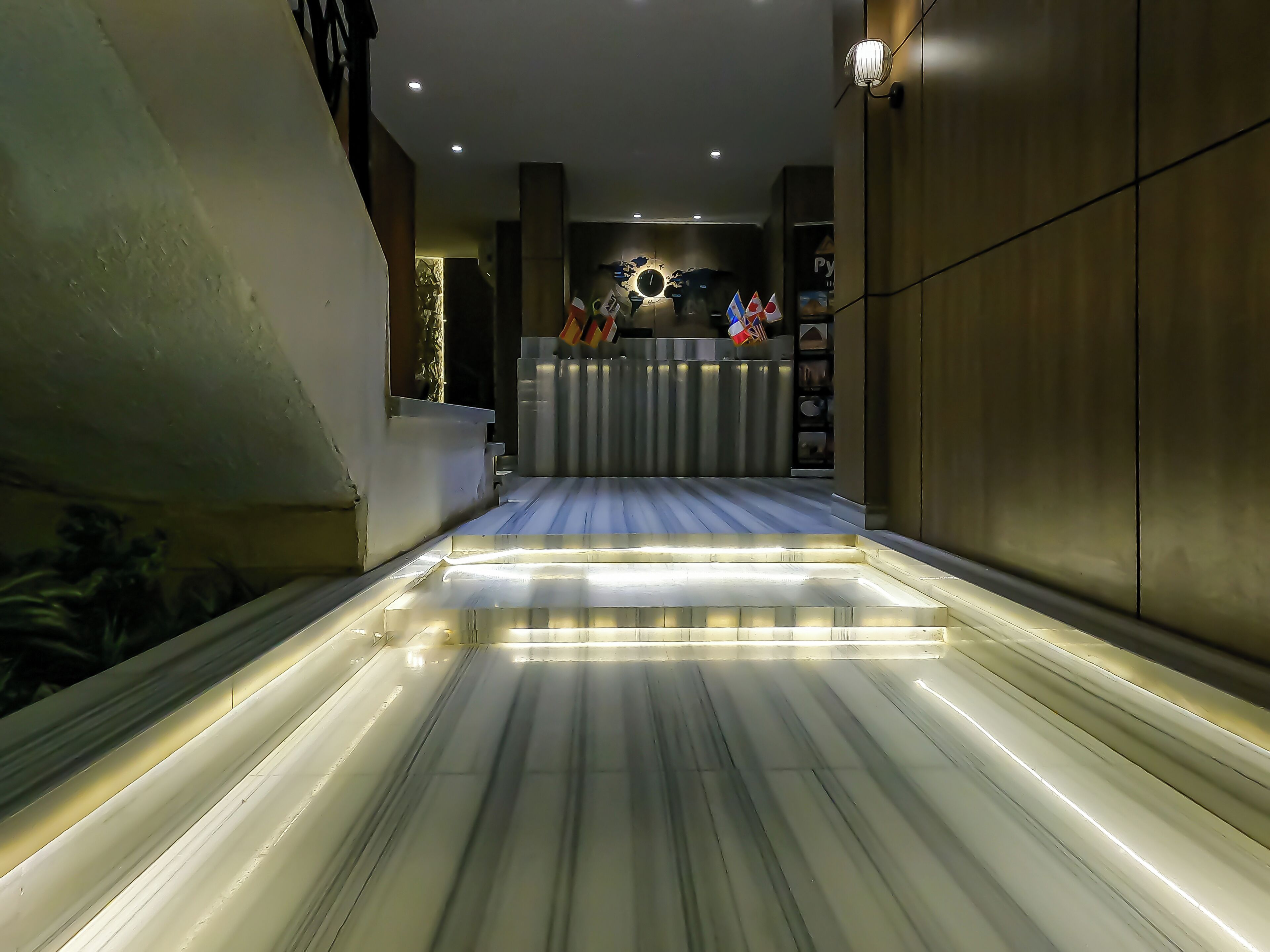A modern hotel lobby with a marble floor, a reception desk, and a wall-mounted clock.